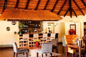 A restaurant with a thatched roof, wooden furniture, and a bar area with bottles. - Bikos Villa (Magaliesberg)
