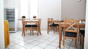 A dining area with wooden tables and chairs, a refrigerator, and a window with a view. - Appartement Hexenhäuschen, 1-3 Pers (Haltern am See)