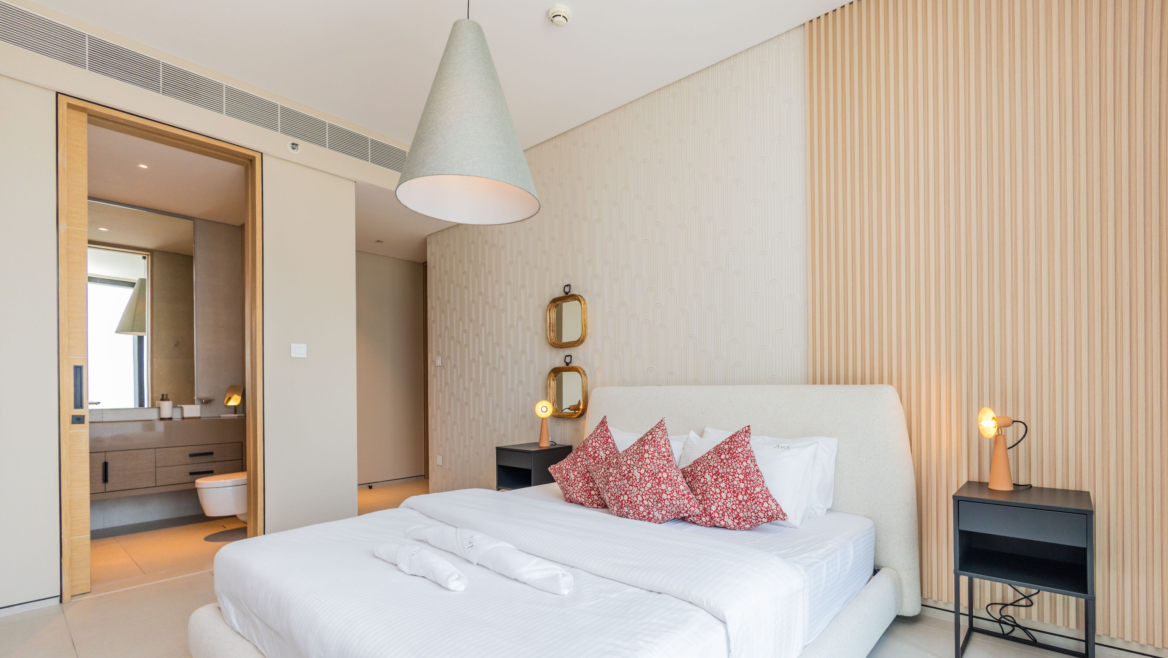 A modern hotel room with a large bed, a bedside table with a lamp, a mirror, and a wall with vertical stripes.