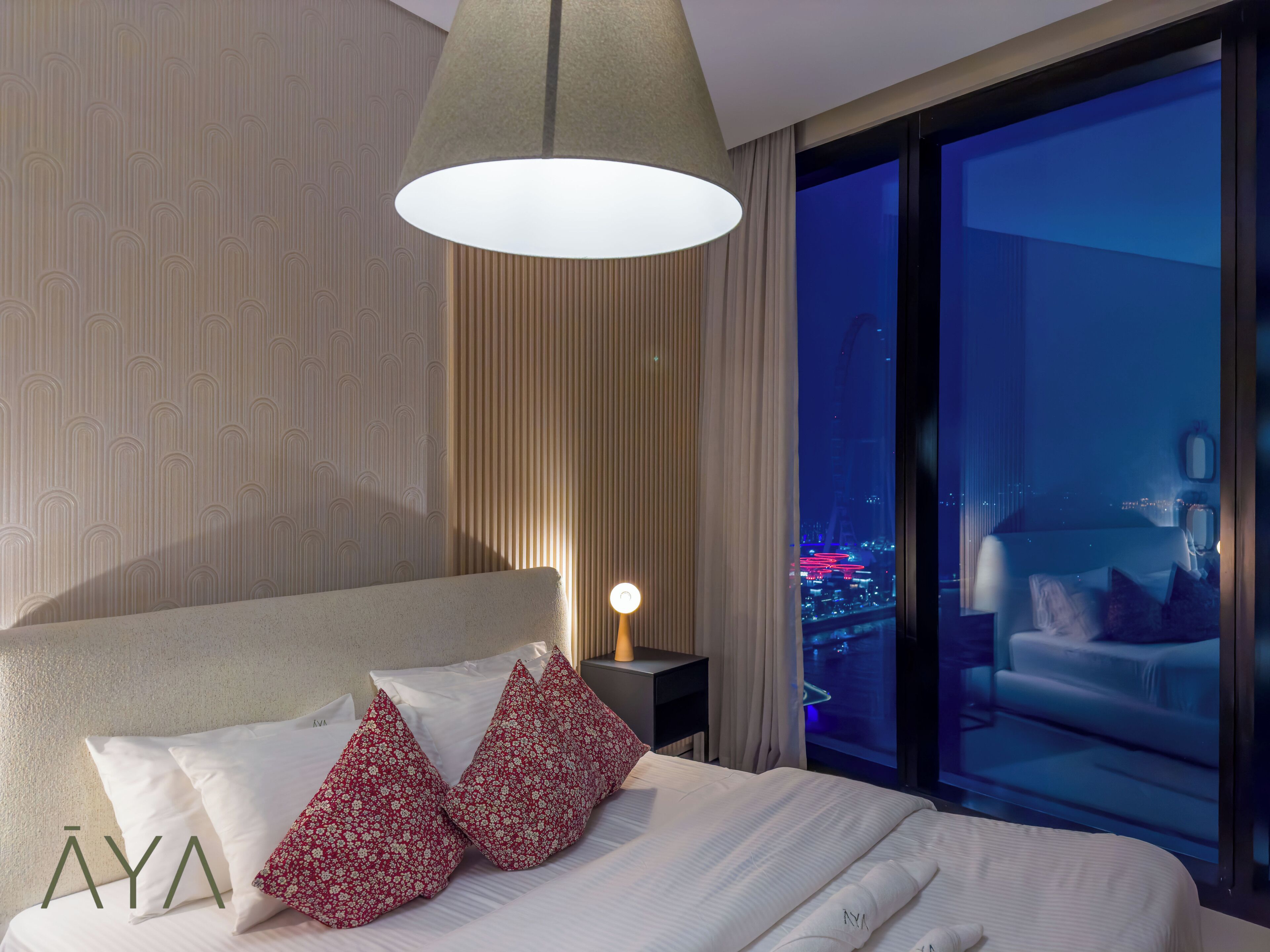 Hotelkamer met een groot bed, nachtkastje, lamp en uitzicht op de stad 's nachts.