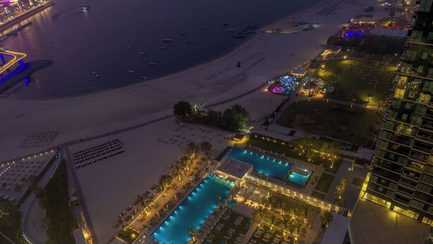 An aerial view of a resort with a large swimming pool, beach access, and a high-rise building. - Aya - Beachfront Bliss 2BR Haven at The Beach Residences (Dubai)