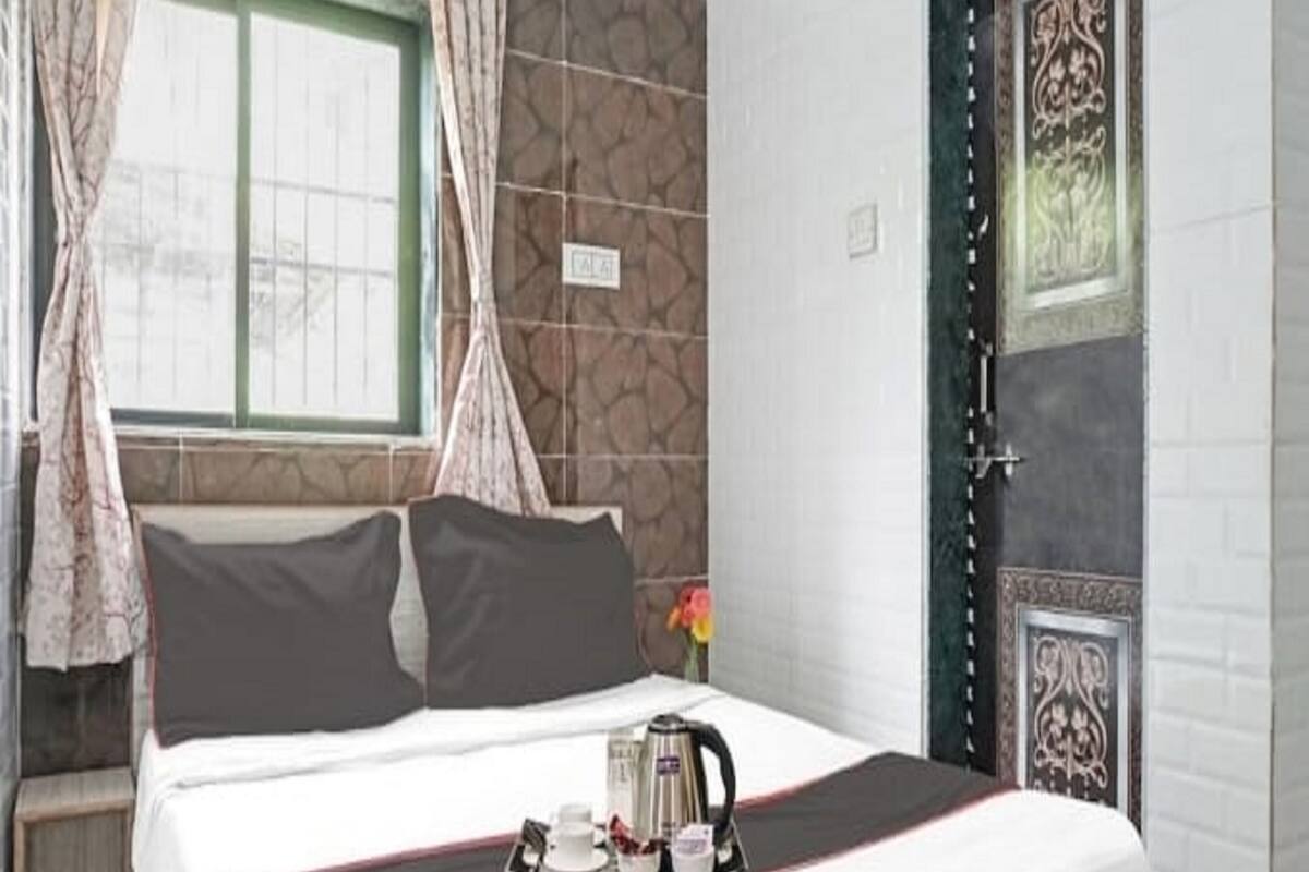 A neatly made bed with a tray of tea and cups, a window with curtains, and a decorative door.