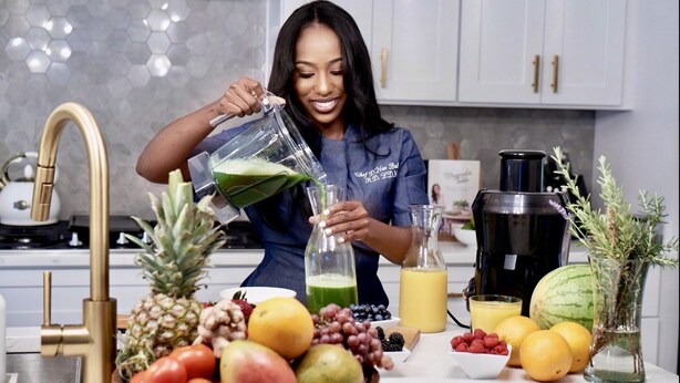 A kitchen with a person pouring a green liquid into a bottle, surrounded by various fruits and a juicer. - Loft Style Spacious Lux Apt 203, sleeps 6 (Atlanta)