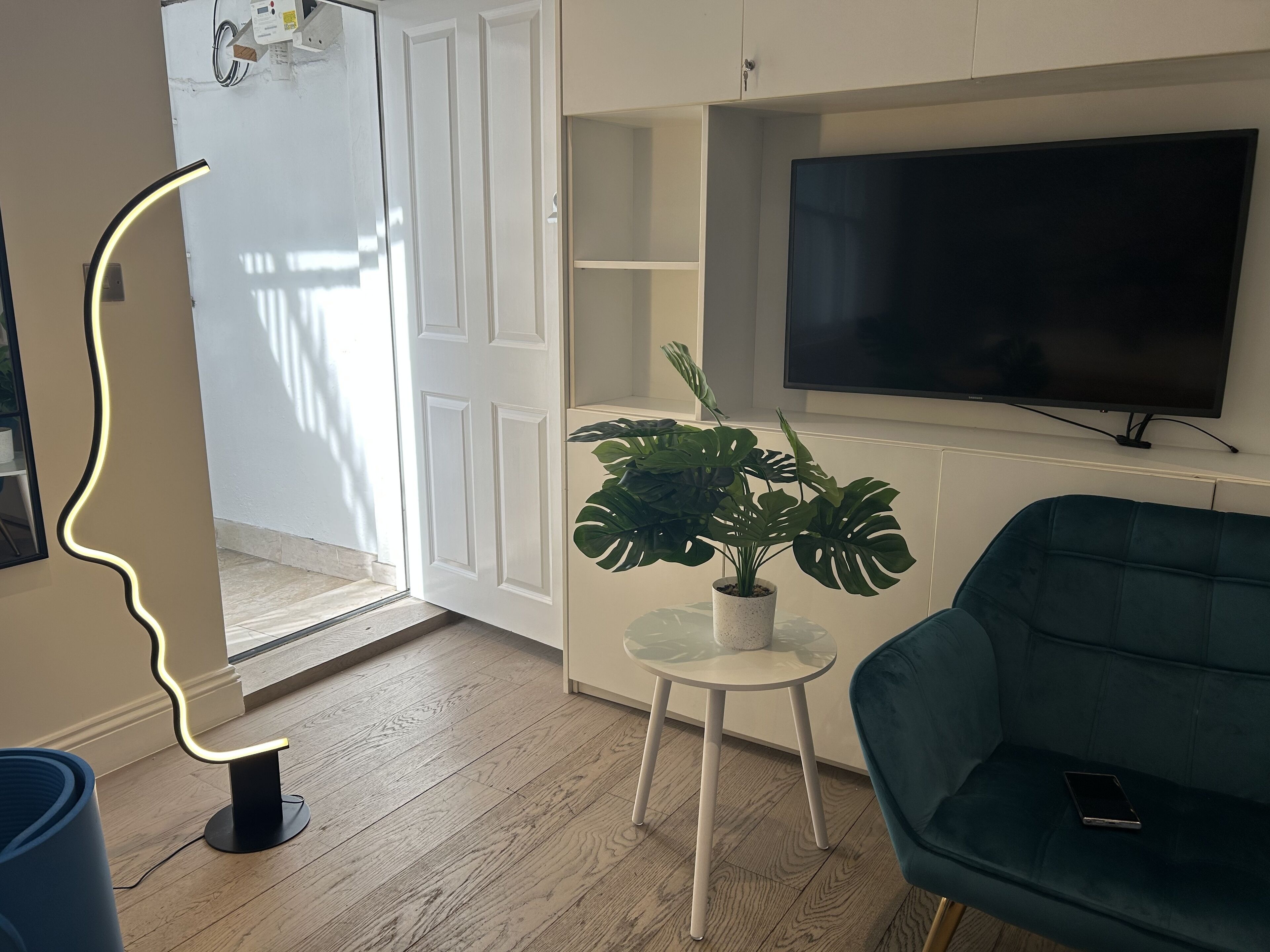 A modern living room with a flat-screen TV, a green sofa, a small white table with a plant, and a unique wall light.