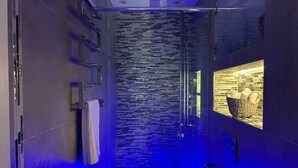 A modern bathroom with a glass shower enclosure, a tiled wall with a pattern, and a basket of towels on a shelf. - Pop Art Luxury Room Marylebone  (London)