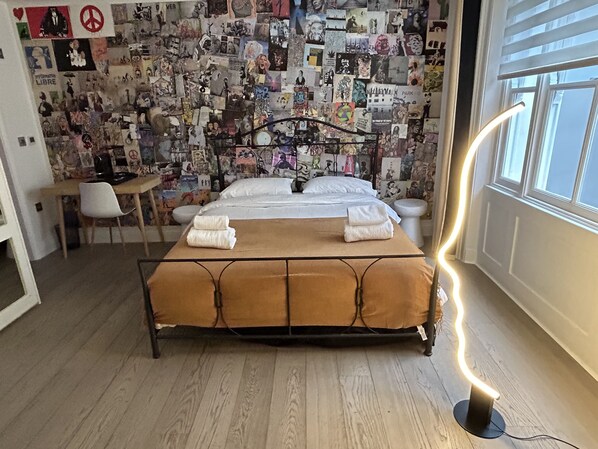 A bedroom with a bed, a desk, and a wall covered with various pictures. - Pop Art Luxury Room Marylebone  (London)