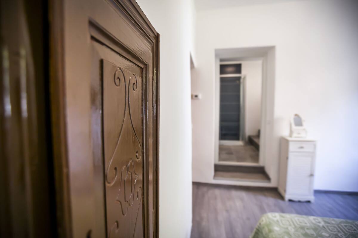 A room with a wooden door, a mirror, a white dresser, and a patterned bedspread.