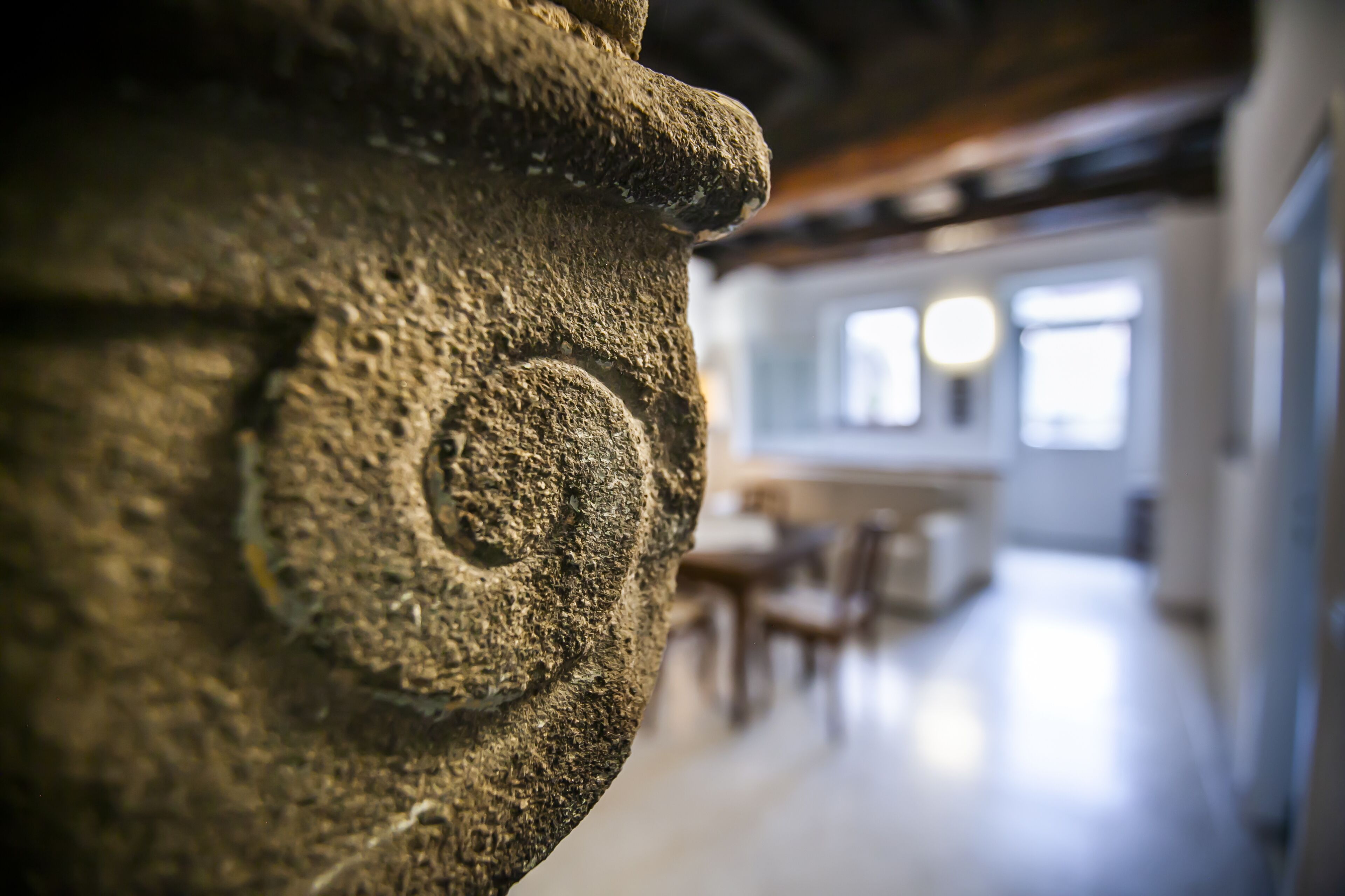 A stone fireplace with a carved design, a dining area with tables and chairs, and a bright interior with natural light.