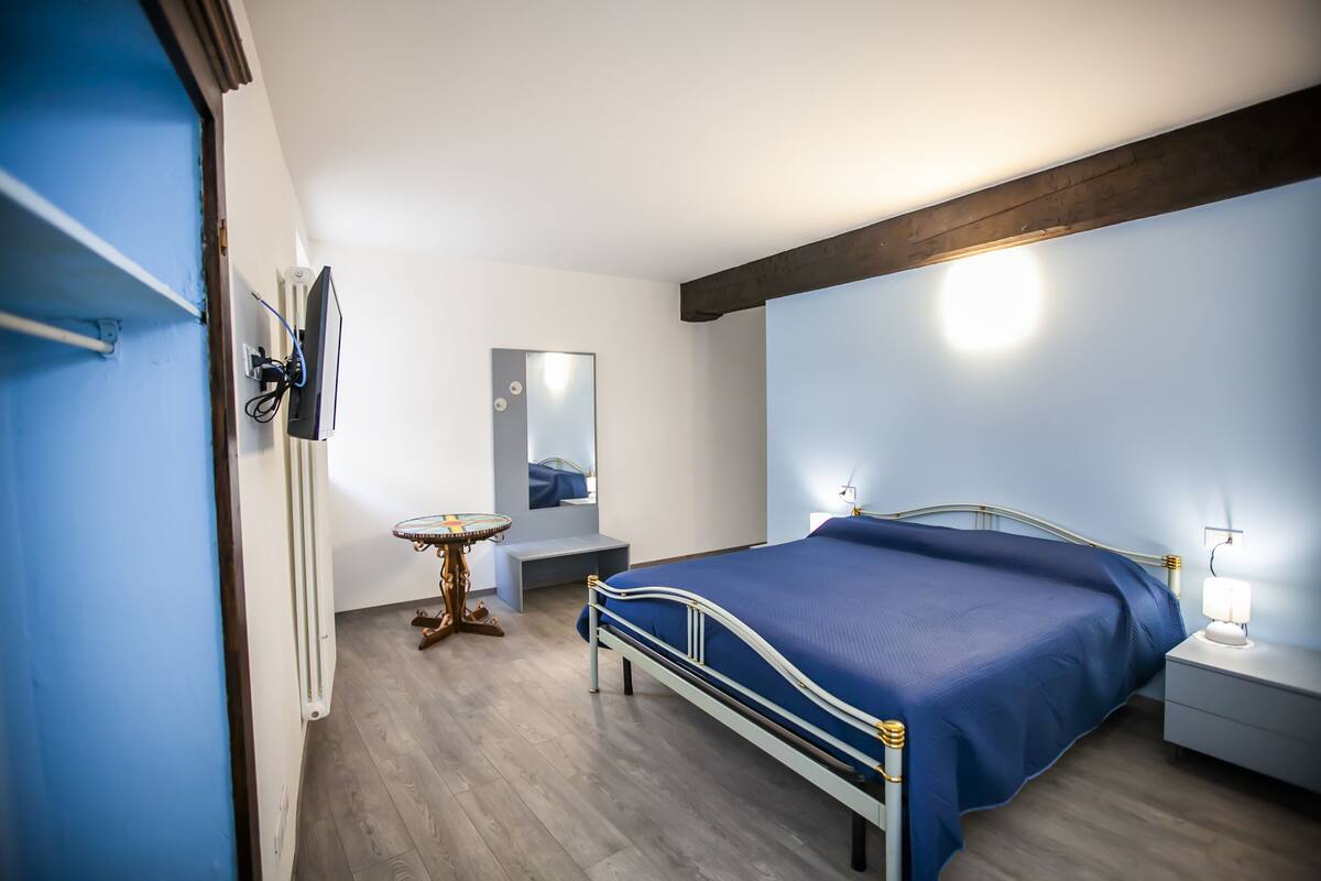 A bedroom with a bed, bedside table, lamp, and a small round table with a mirror.