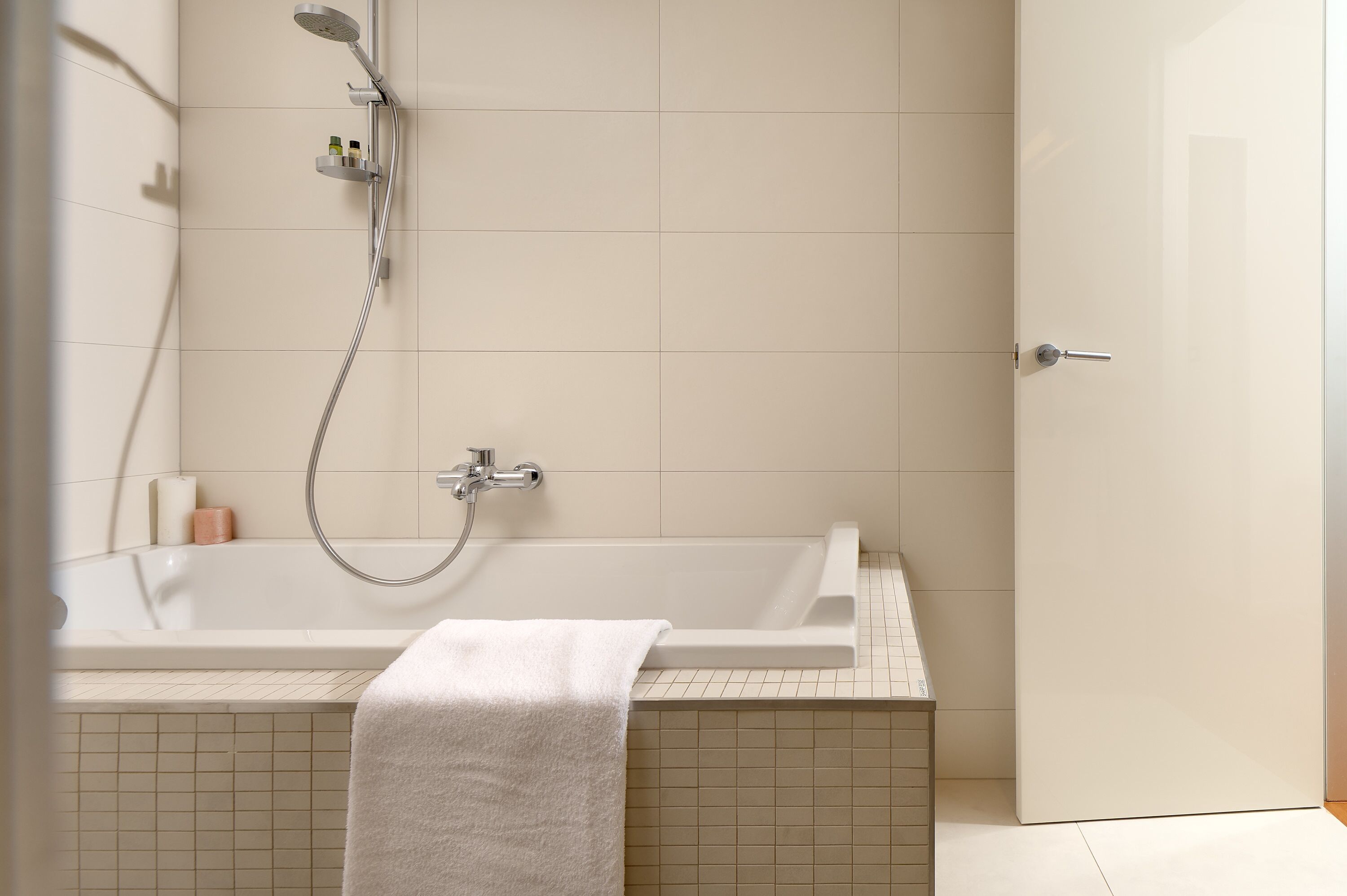 A modern bathroom with a bathtub, a showerhead, and a towel on the floor.