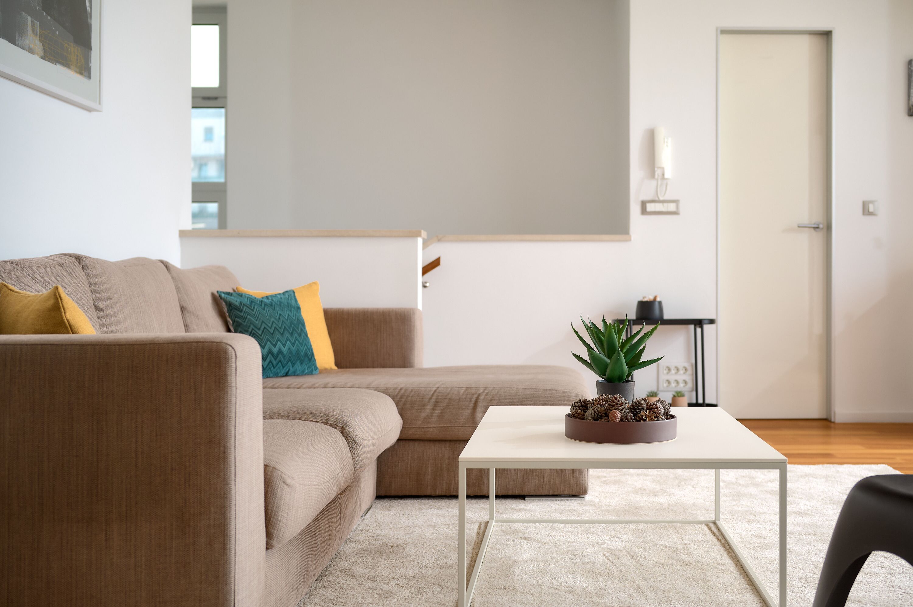 A modern living room with a beige sofa, a white coffee table, and a small plant.