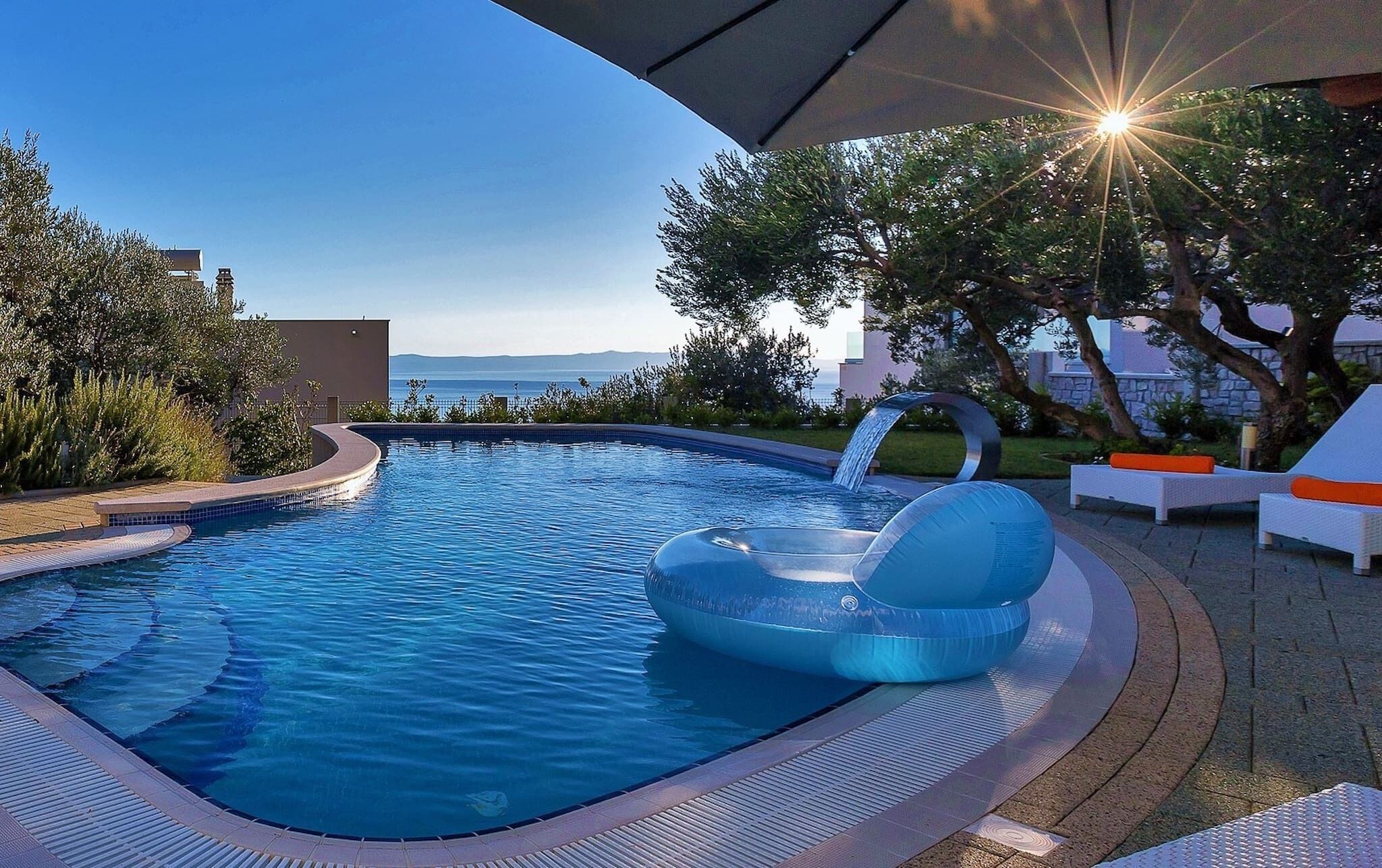 A swimming pool with a water slide, lounge chairs, and a view of the sea.