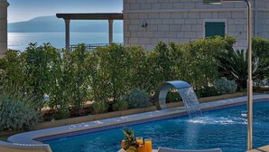 Une piscine agrémentée d’une cascade, entourée d’une végétation luxuriante et offrant une vue sur la mer.