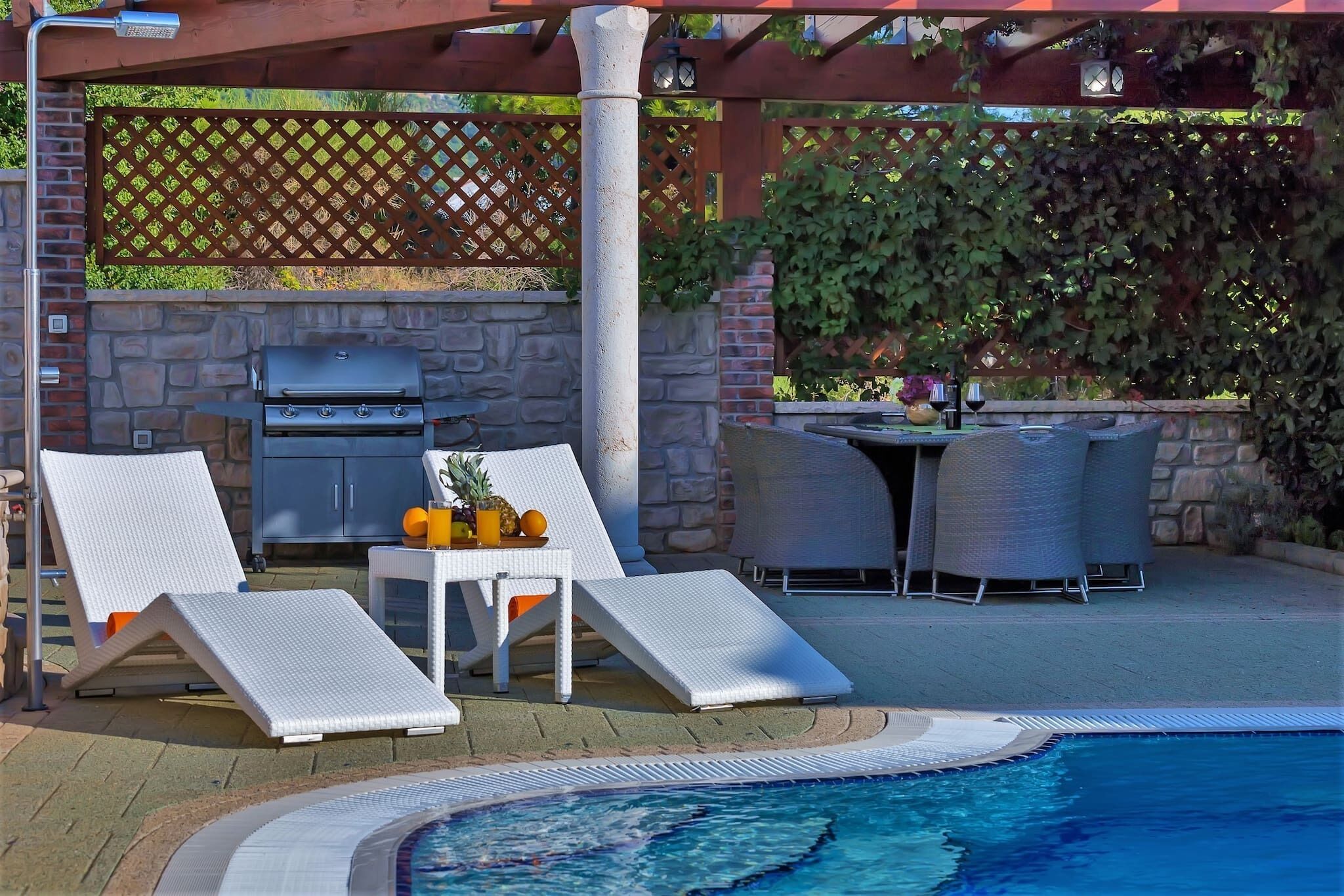 A poolside area with lounge chairs, a grill, and a table with drinks.