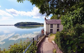 A lakeside property with a white building, a paved pathway, and a fence.
