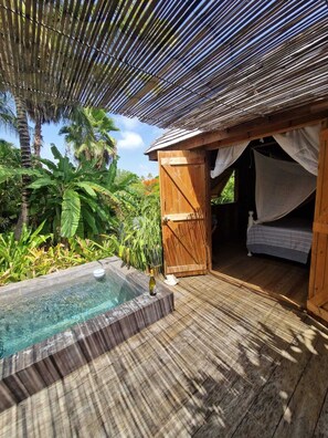 Une terrasse en bois avec un jacuzzi, un auvent et un lit doté d’une moustiquaire.