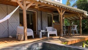 Ein Poolbereich mit Holzterrasse, weißen Stühlen und einer überdachten Sitzgelegenheit.