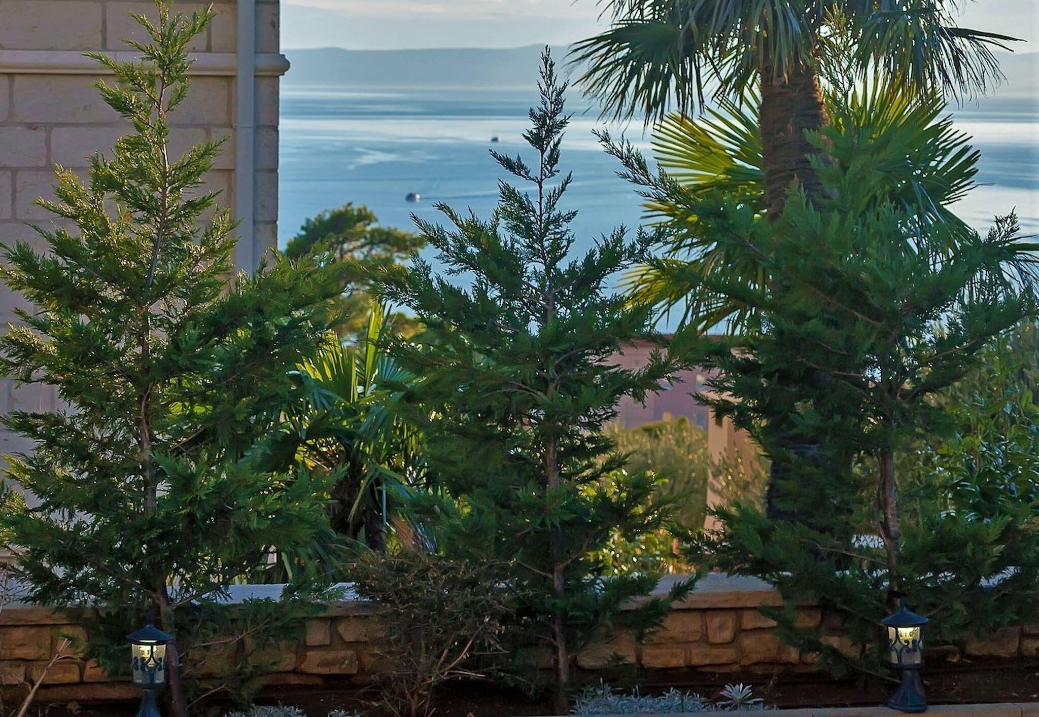 A view of a landscaped area with trees and a stone wall, overlooking a body of water.