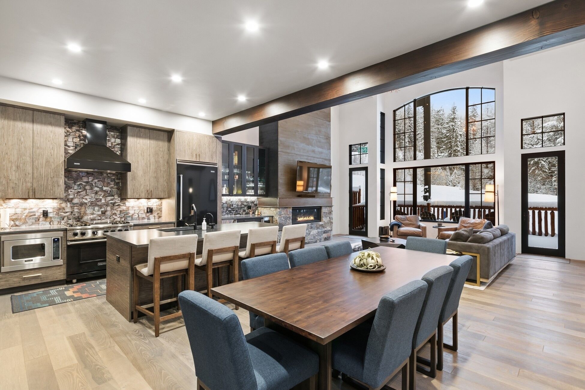 Une cuisine moderne avec un mur de crédence en pierre, un grand îlot central et un coin repas avec des chaises bleues.