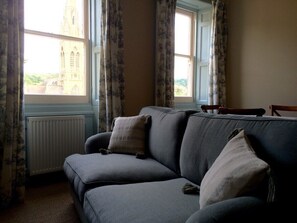 Ein Zimmer mit grauem Sofa, Heizkörper und einem mit Vorhängen versehenen Fenster.