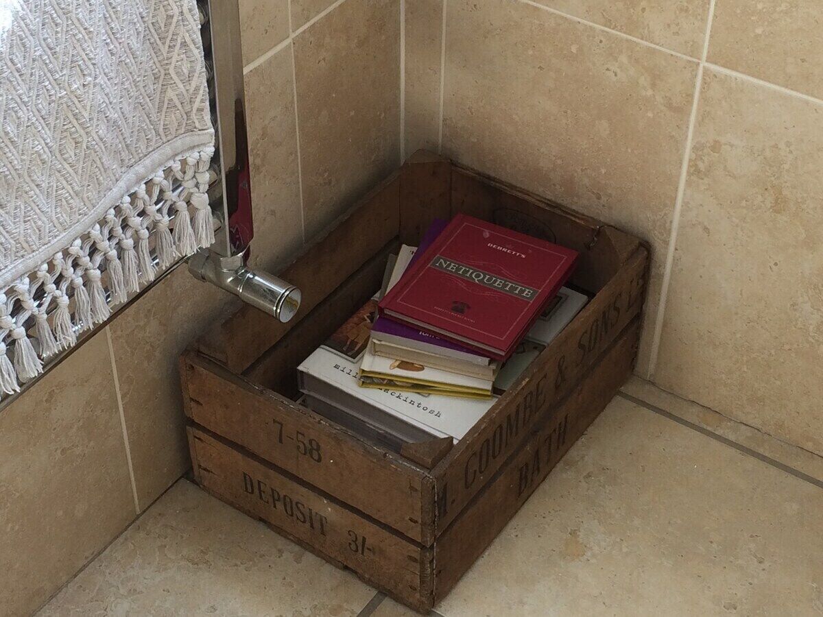 Een houten kist met boeken, een metalen voorwerp en een decoratieve wandhanger in een hoek.