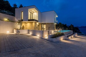 A modern two-story house with a swimming pool, large windows, and a well-lit exterior. - Luxury Villa Luce, right on the beach (Potomje)