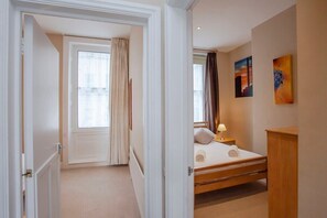 A hotel room with a bed, a nightstand, a window with curtains, and artwork on the wall. - Great City Centre Apartment (GS) (Bath)