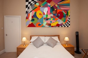 A hotel room with a bed, two bedside tables with lamps, a large abstract painting on the wall, and a standing heater. - Great City Centre Apartment (GS) (Bath)