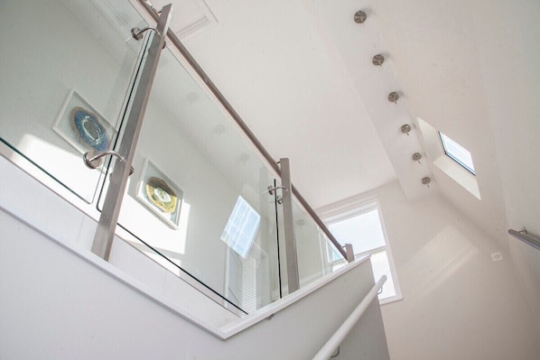 A modern interior with a glass railing, a ceiling with recessed lighting, and a window with blinds.