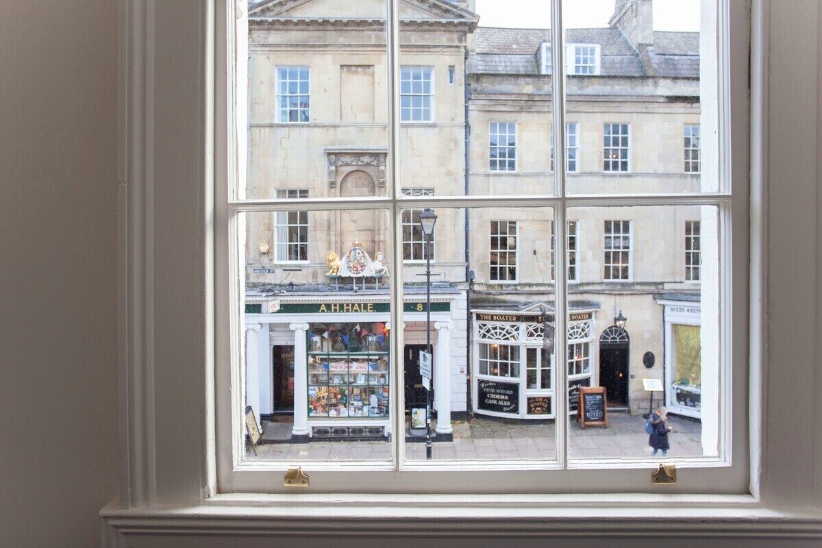 A view through a window of a street scene with buildings, including a shop with a sign 'A.H. Hale' and another with a sign 'The Boater.'
