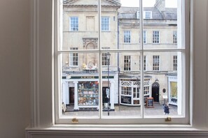Une vue à travers une fenêtre sur une scène de rue, avec des bâtiments, dont une boutique portant l’enseigne « A.H. Hale » et une autre avec l’enseigne « The Boater ».