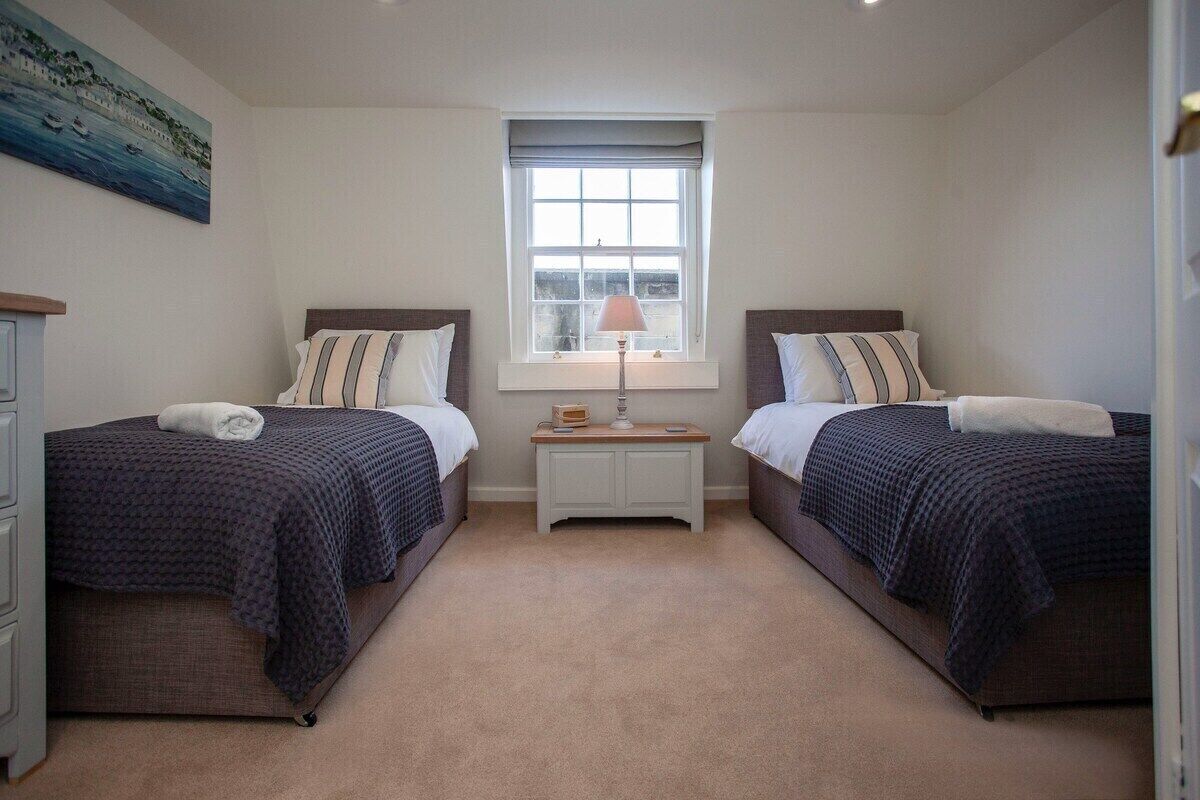 A bedroom with two beds, a nightstand, a window, and a painting on the wall.