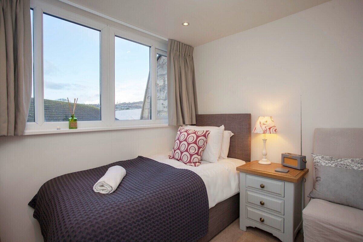 A hotel room with a bed, bedside table, lamp, and a window with curtains.