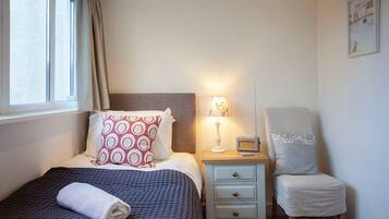 A neatly made bed with a patterned pillow, a bedside lamp, a chair with a lace cover, and a small table with a radio.