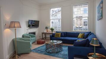 A living room with a blue sofa, a glass coffee table, a floor lamp, and a television.