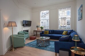 A living room with a blue sofa, a glass coffee table, a floor lamp, and a television.