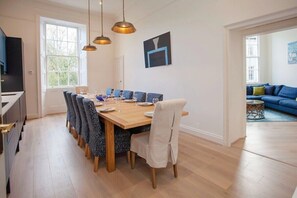 A dining area with a wooden table and chairs, a television, and a sofa in the adjacent room. - Stunning, Bath Townhouse, City Centre (AS) (Bath)
