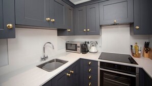 Een moderne keuken met donkere kastjes, roestvrijstalen apparatuur en gouden handgrepen.