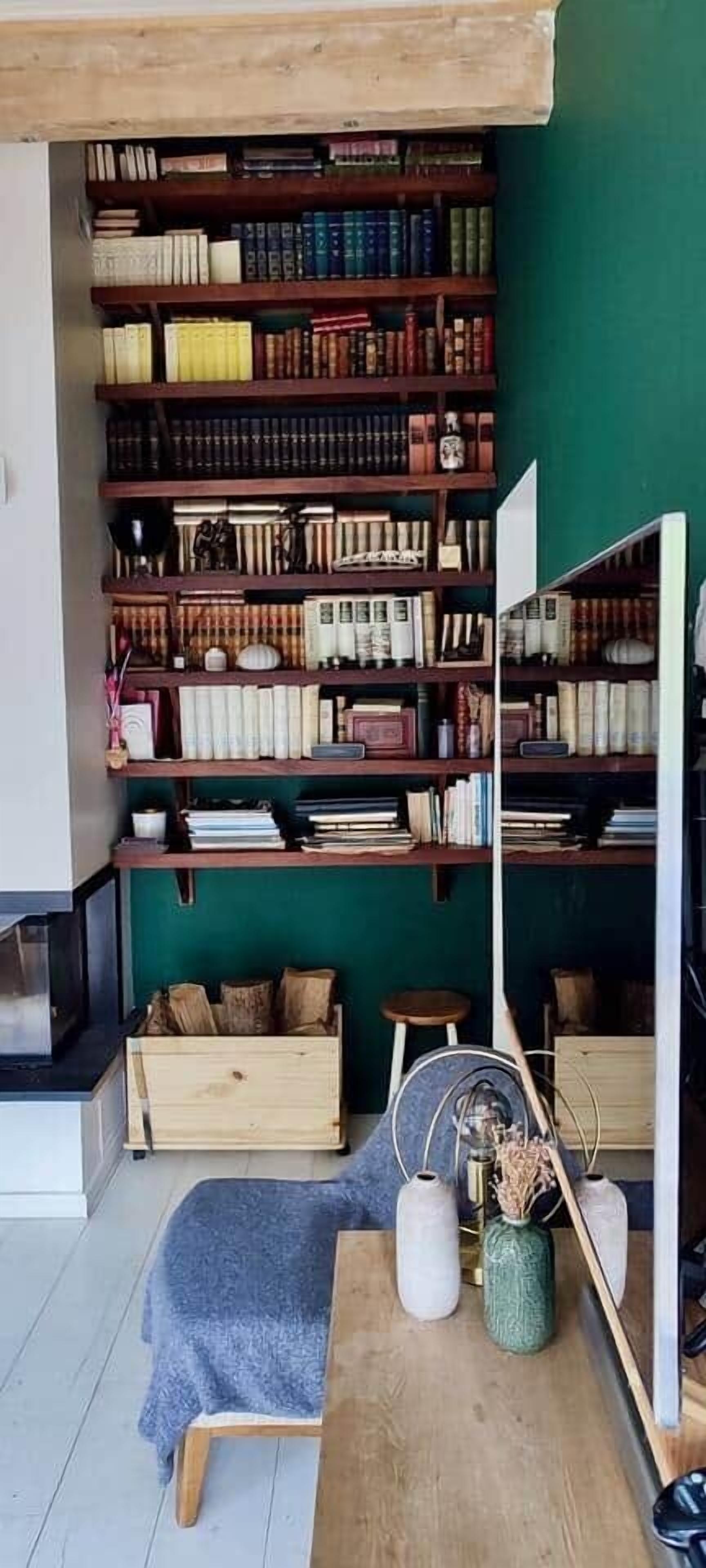 Une pièce avec une bibliothèque, une table en bois et un mur vert.