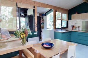 A compact kitchen with teal cabinets, a wooden dining table, and a vase of flowers.