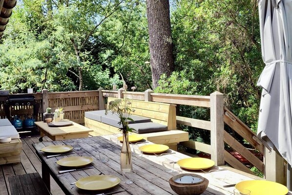 An outdoor deck with wooden furniture, a grill, and a wooden fence.