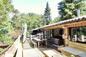 A wooden deck with a table and benches, a covered seating area, and a view of a forested area.
