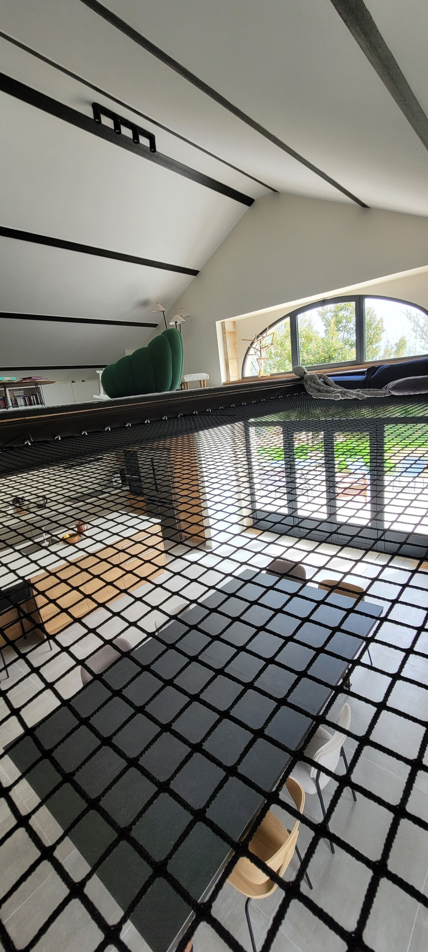 Ein modernes Zimmer mit schwarzem Rasterboden, einem grünen Sessel und Blick ins Freie durch ein großes Fenster.