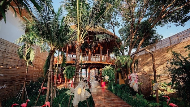 A tropical resort with a wooden structure, a thatched roof, and a pathway lined with tropical plants and flamingos. - 75/2 Residence Hua Hin (Hua Hin)
