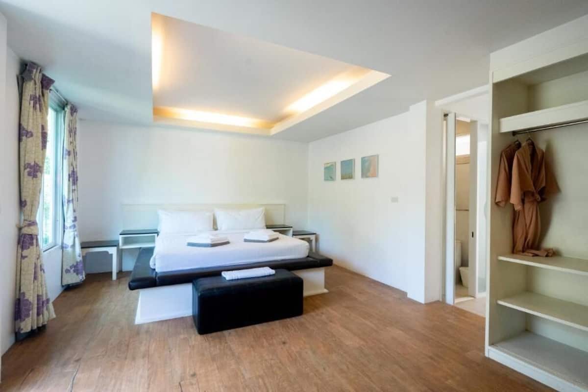 A modern bedroom with a bed, bedside tables, a bench, and a walk-in closet.