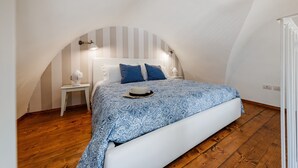 Ett sovrum med ett sluttande tak, en säng med ett mönstrat överkast, två sängbord med lampor och ett trägolv.