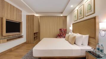 Una habitación de hotel moderna con una cama grande, un televisor de pantalla plana montado en la pared, un sillón estampado y un cabecero de madera.