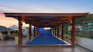 A rooftop swimming pool with a wooden pergola, lounge chairs, and potted plants.