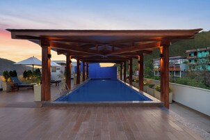 Piscina en la azotea con una pérgola de madera, sillas de descanso y plantas en macetas.