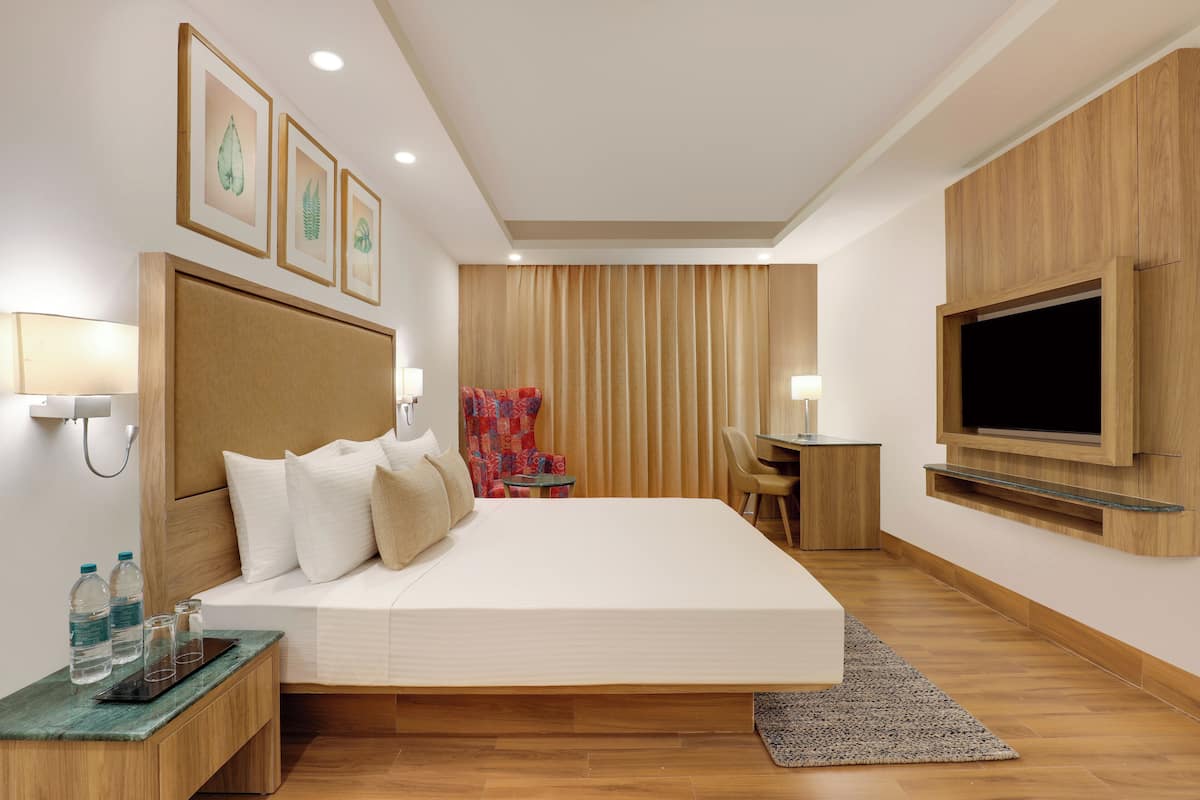 A modern hotel room with a large bed, a TV mounted on the wall, a desk with a chair, and framed pictures on the wall.